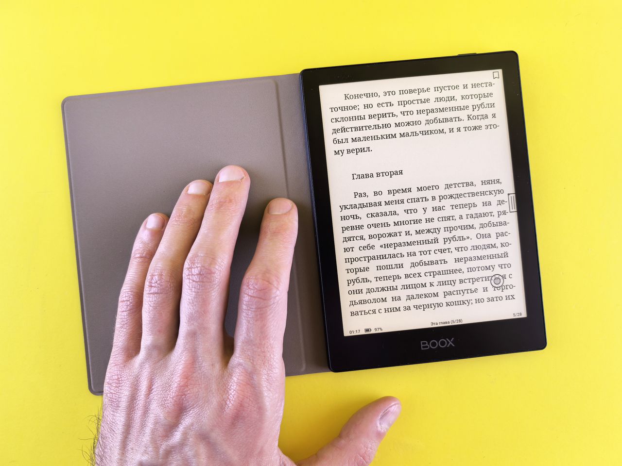 social-feed-img-02 A hand holding an e-reader displaying text on a bright yellow background, showcasing modern digital reading.