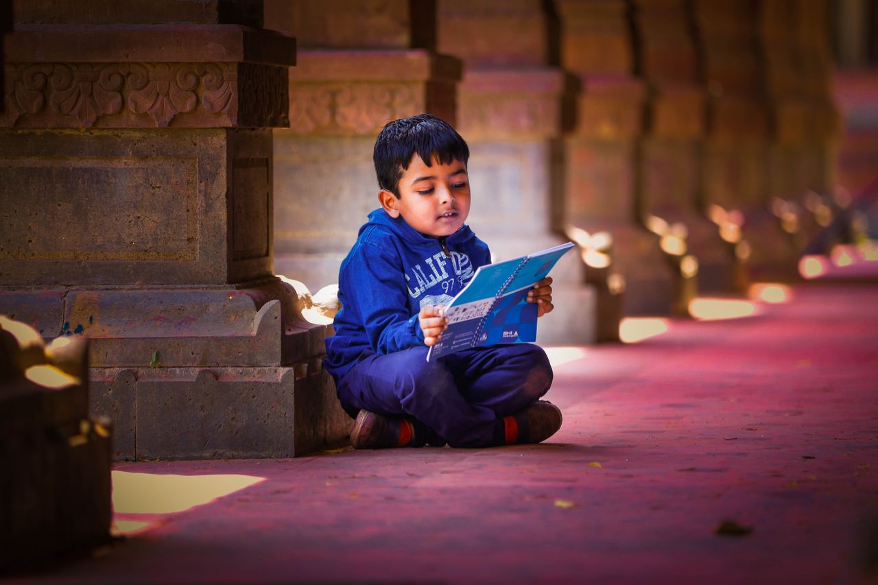 A young boy sits and reads a book indoors in a traditional Indian architectural setting in Indore.