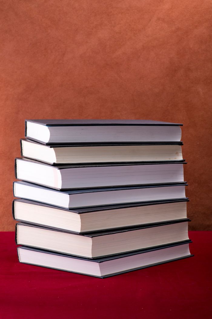 social-feed-img-04 Stacked hardcover books on a red table and brown background creating a classic academic vibe.