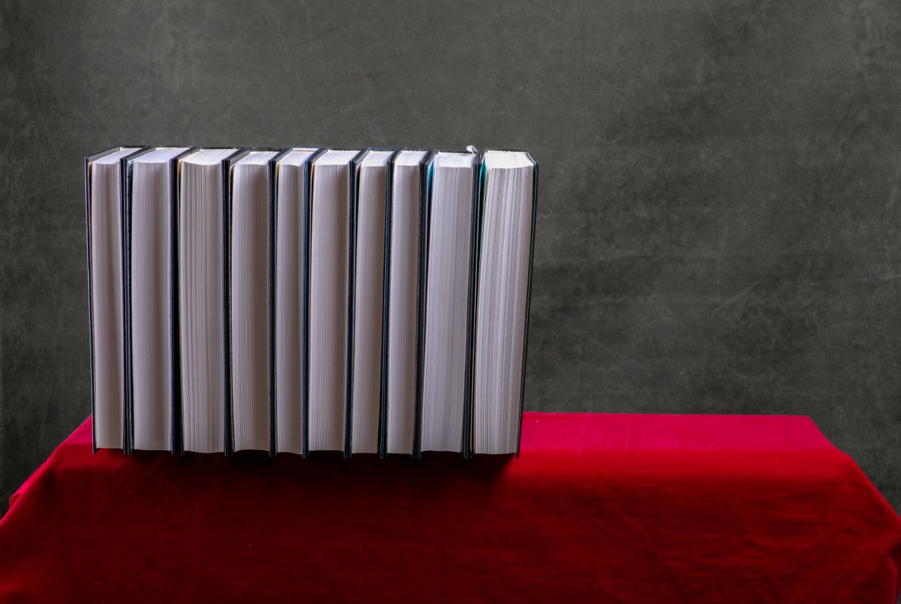 best-selling product-02 A row of books lined up on a red tablecloth, against a textured gray backdrop.